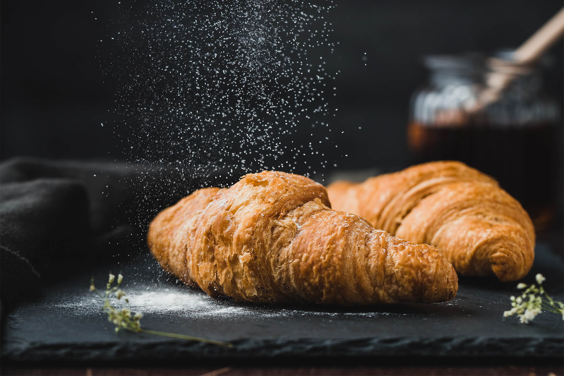 Two French croissants dusted with powdered sugar on a slate board