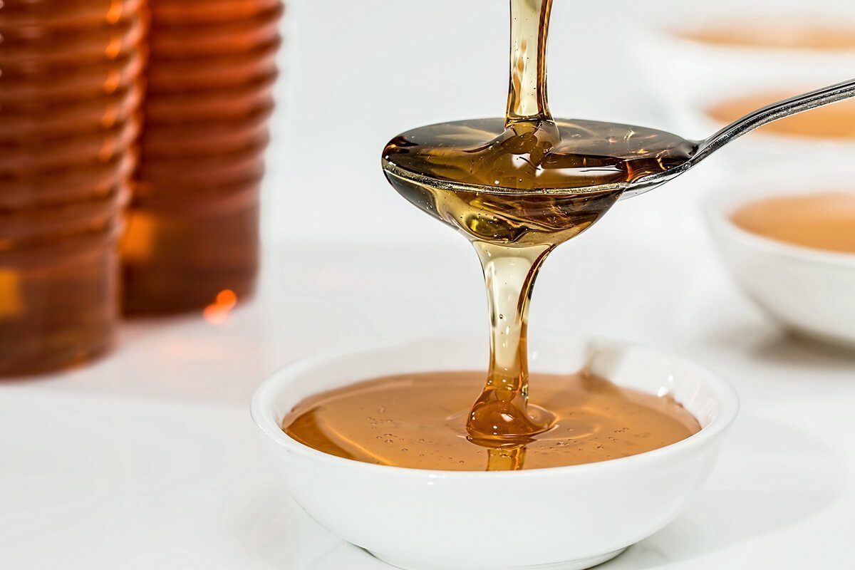 Amber honey flowing into a spoon and a small goblet on the side.